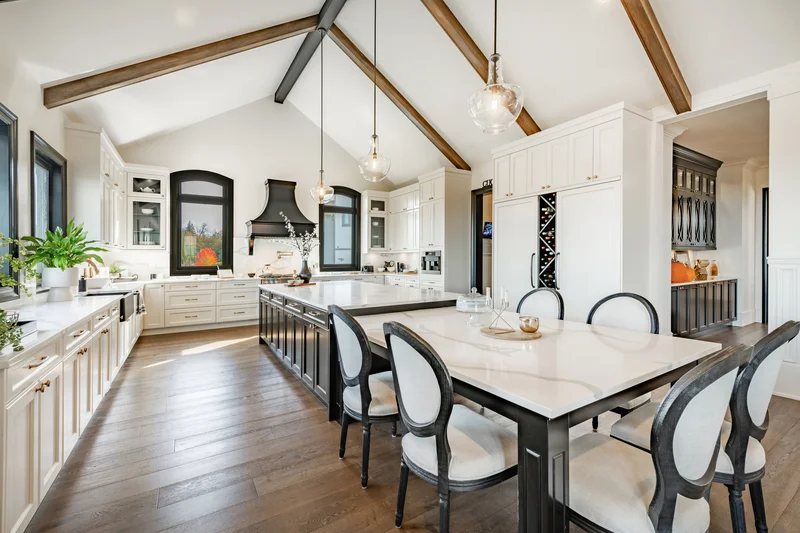 Spacious white kitchen with vaulted wood beams and dining table